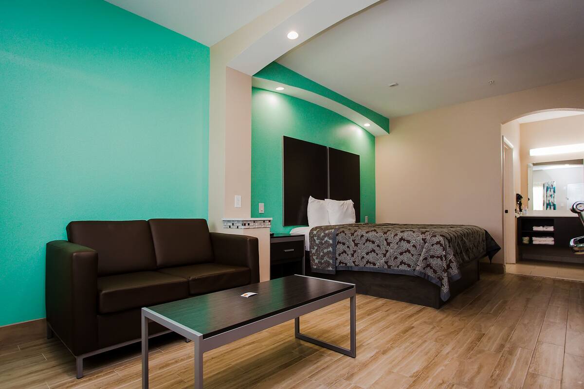 Une chambre d’hôtel avec un canapé marron, un lit recouvert d’une couvre-lit à motifs, une petite table et un mur d’accent vert.