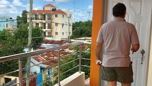 Ein Mann geht auf einem Balkon mit Blick auf Gebäude und einen klaren Himmel.