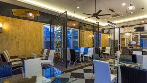 A modern indoor space with glass tables and chairs, a ceiling fan, and a view through a glass partition. - Palmchwa Resort (Sikhio)