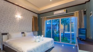 A modern bedroom with a large bed, a flat-screen TV, and a sliding glass door leading to a garden. - Palmchwa Resort (Sikhio)