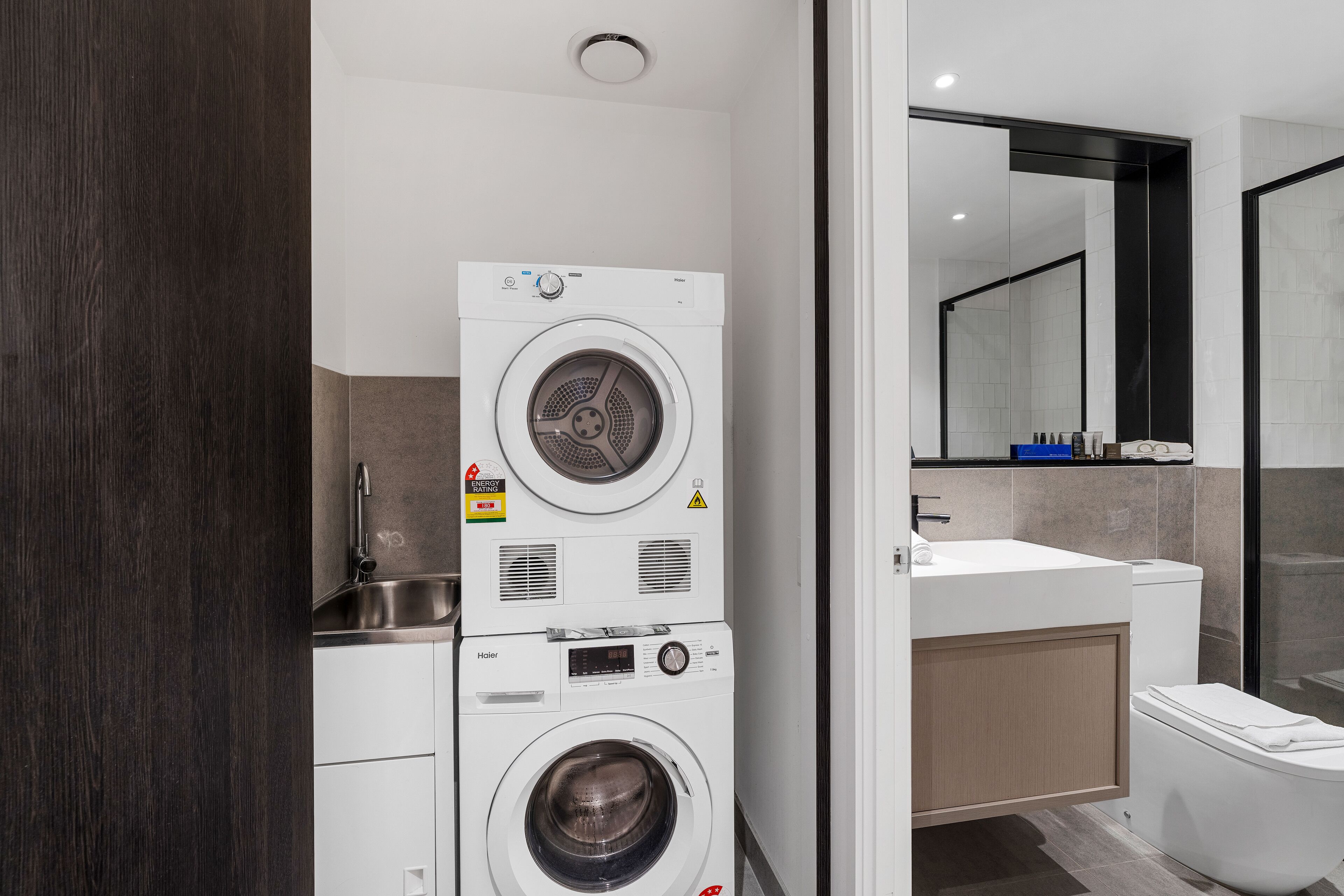Un bany modern amb rentadora i assecadora apilades, un lavabo i un vàter.