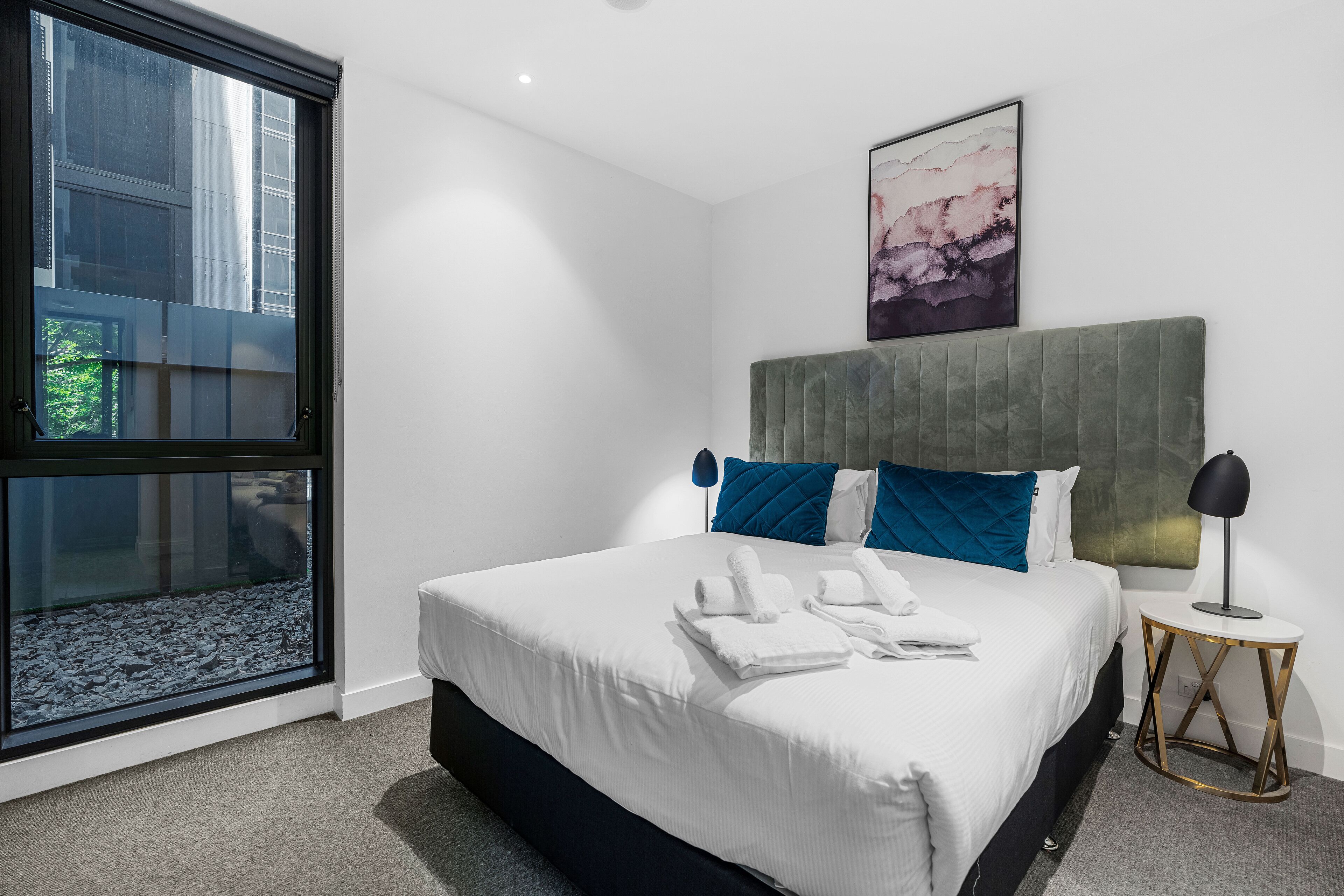 Een moderne hotelkamer met een groot bed, uitzicht door een raam en een schilderij aan de muur.