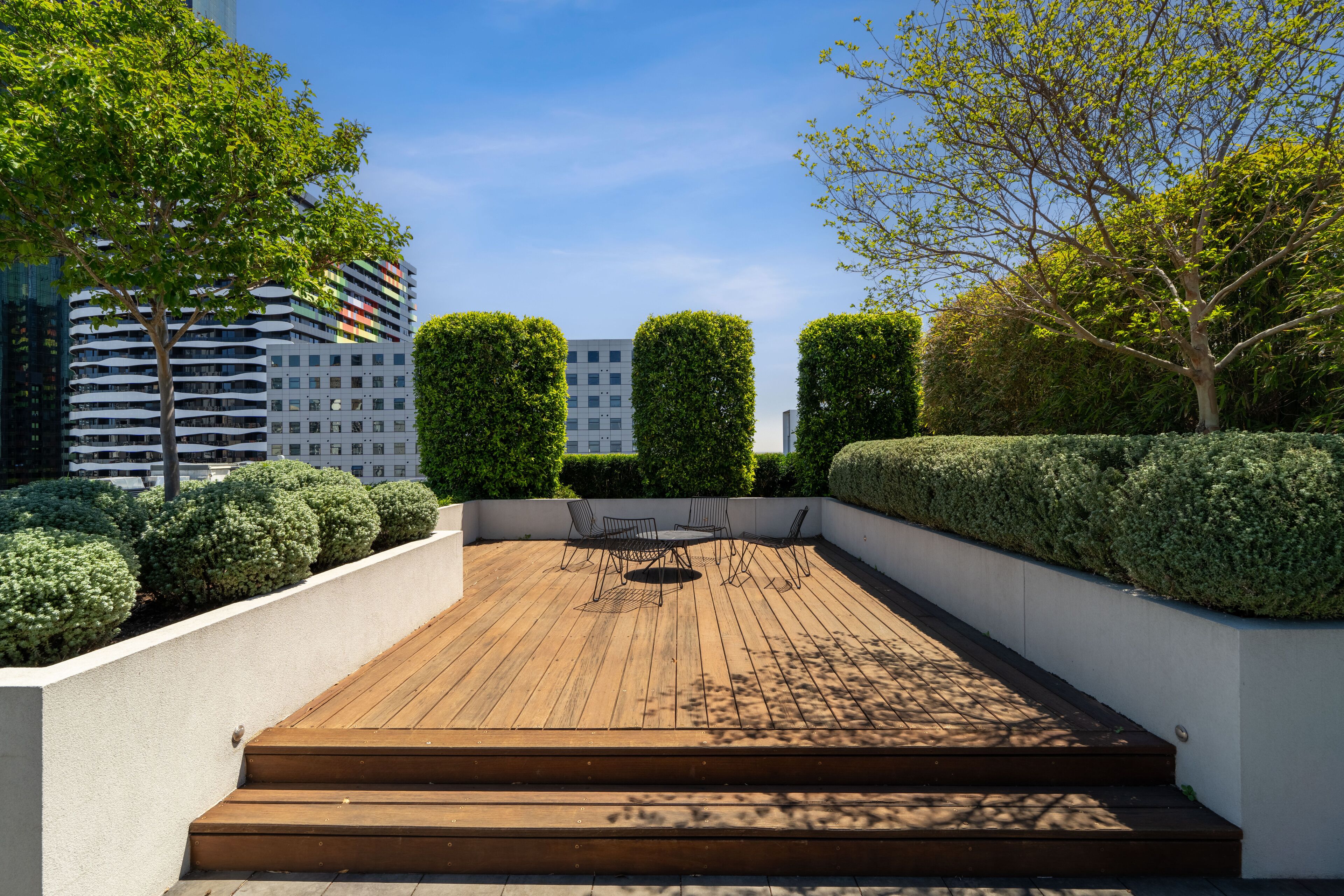 Una terraza en la azotea con piso de madera, una mesa redonda con sillas y setos bien cuidados.