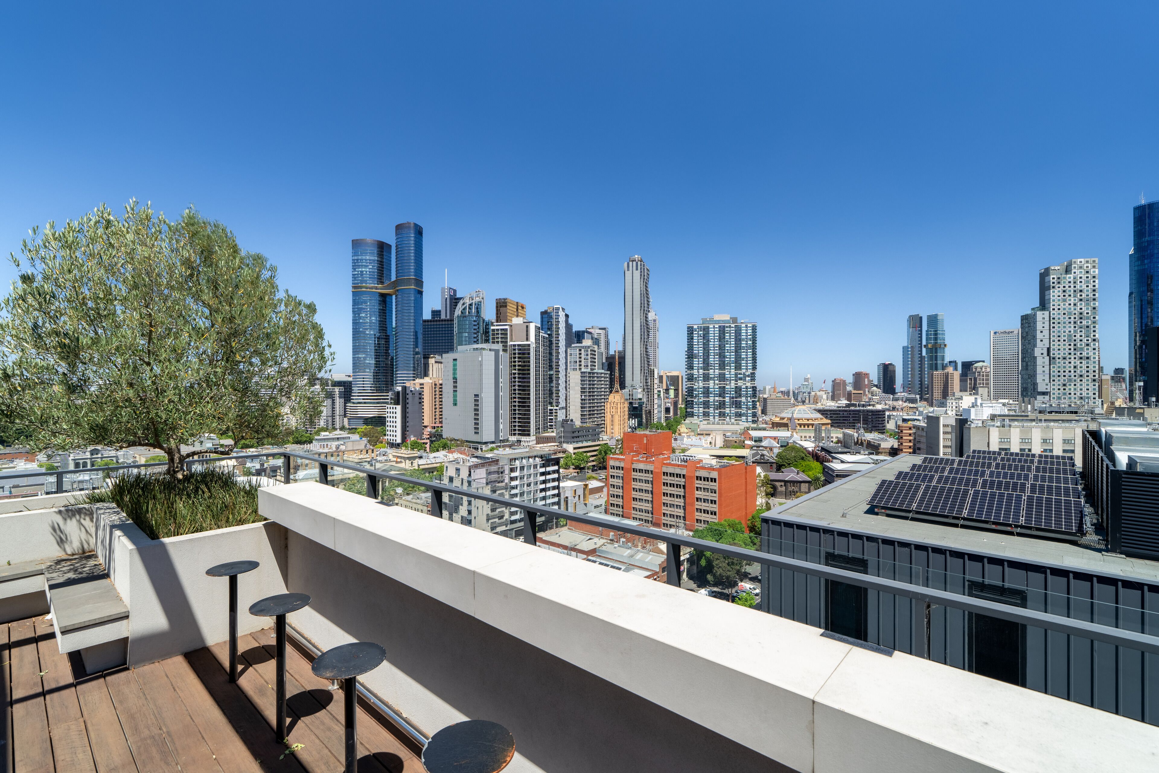 A rooftop terrace with a city skyline view, including modern buildings and a tree.
