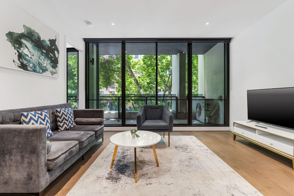 Una sala de estar moderna con un sofá gris, una mesa de centro redonda, un sillón gris y un televisor de pantalla plana.