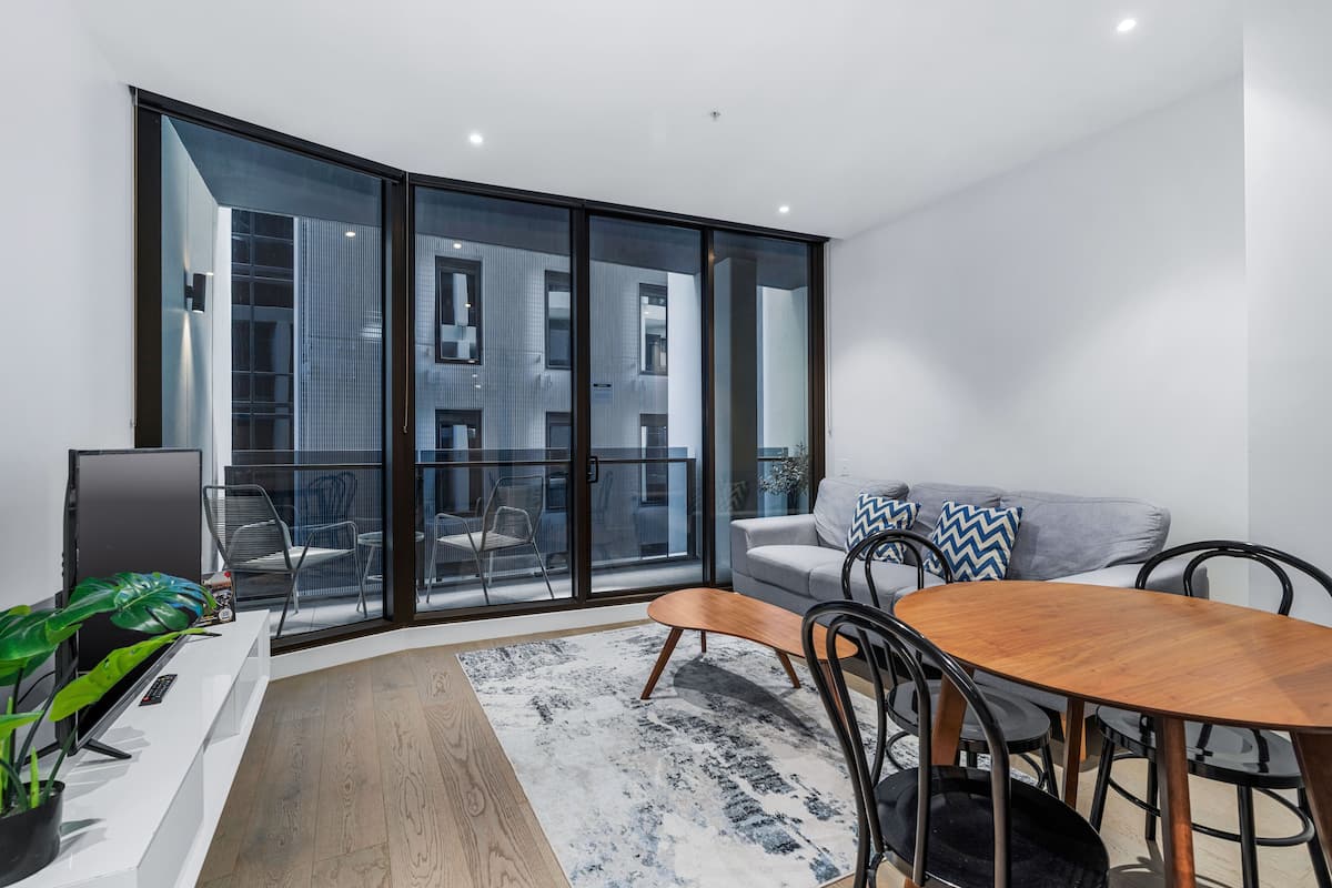 Una sala moderna con comedor, grandes puertas corredizas de vidrio, un sofá gris y una mesa de comedor de madera.