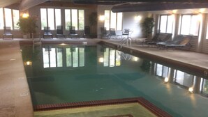 An indoor swimming pool with clear water, surrounded by lounge chairs and a tiled deck.