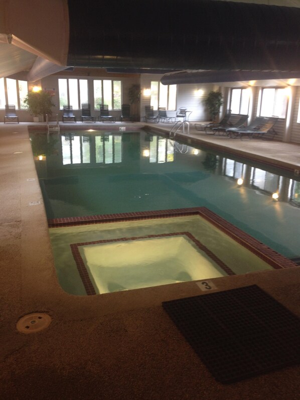 Una piscina interior con agua cristalina, rodeada de sillas de descanso y un solárium con baldosas.