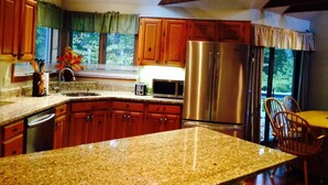 A kitchen with granite countertops, wooden cabinets, a stainless steel refrigerator, and a dining area with a table and chairs.