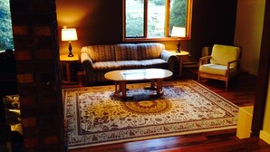 A cozy living room with a sofa, armchair, and coffee table, featuring a large window and a patterned rug.