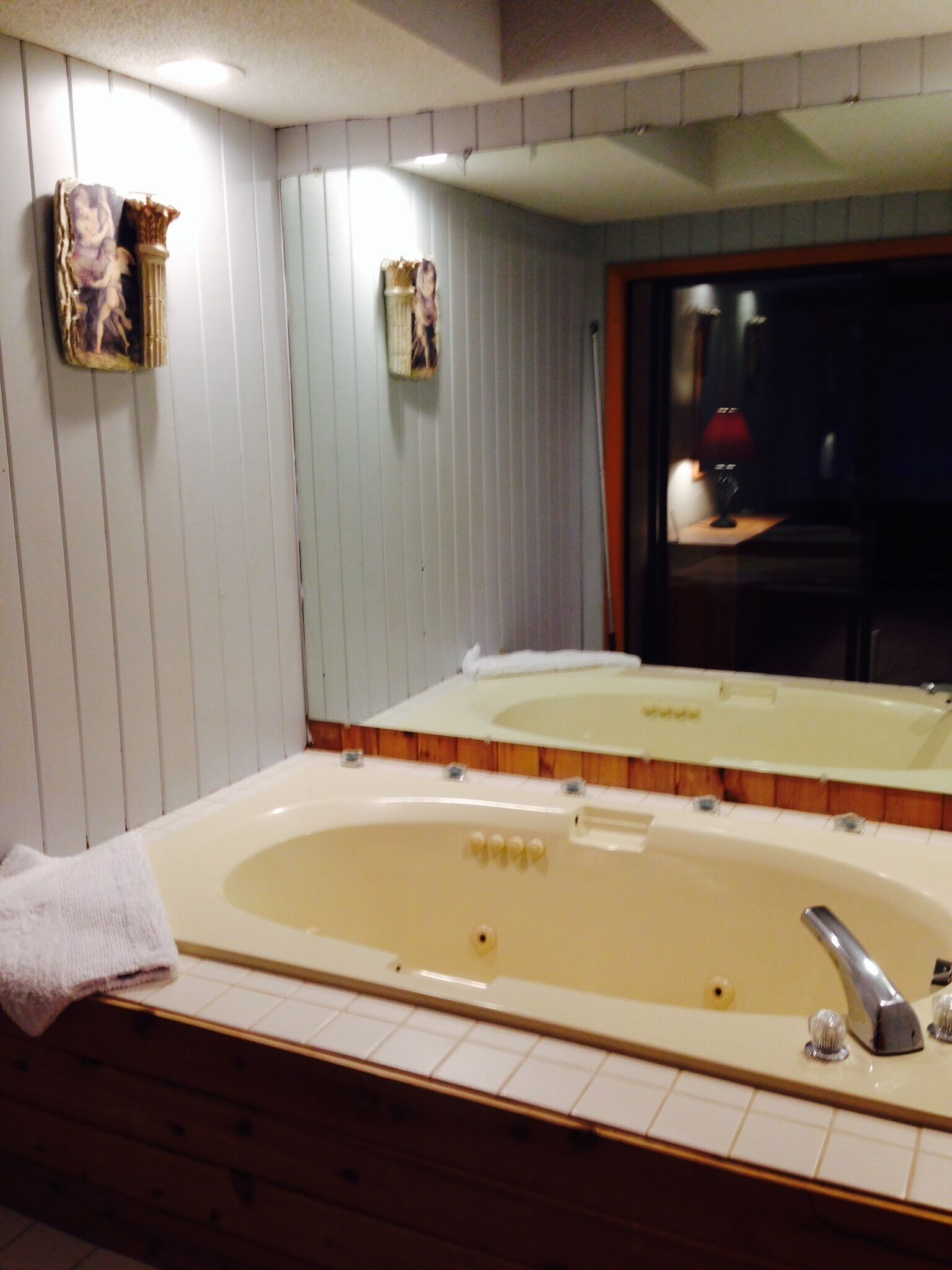 A bathroom with a large bathtub, a mirror, and wooden paneling on the walls.