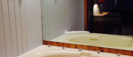 A bathroom with a large bathtub, a mirror, and wooden paneling on the walls.