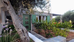 Una casa de piedra con puerta verde, un sendero de piedra y un jardín con diversas plantas y flores.