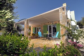 Une terrasse couverte avec un sol en pierre, deux chaises bleues, une table et une pergola.