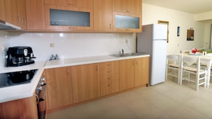 Una cocina con armarios de madera, microondas, refrigerador, cafetera y un comedor con mesa y sillas.