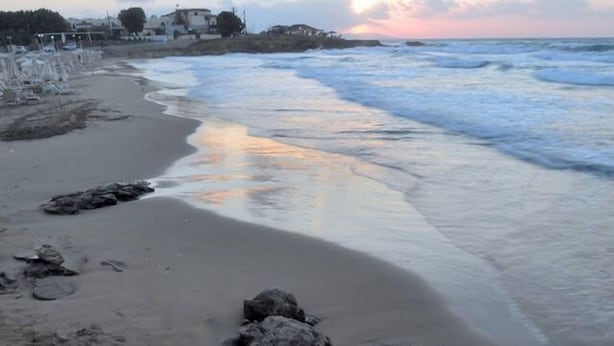 Una playa con olas, rocas y edificios al fondo.