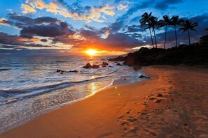 Ein Strand mit Sonnenuntergang, Palmen und Felsen.