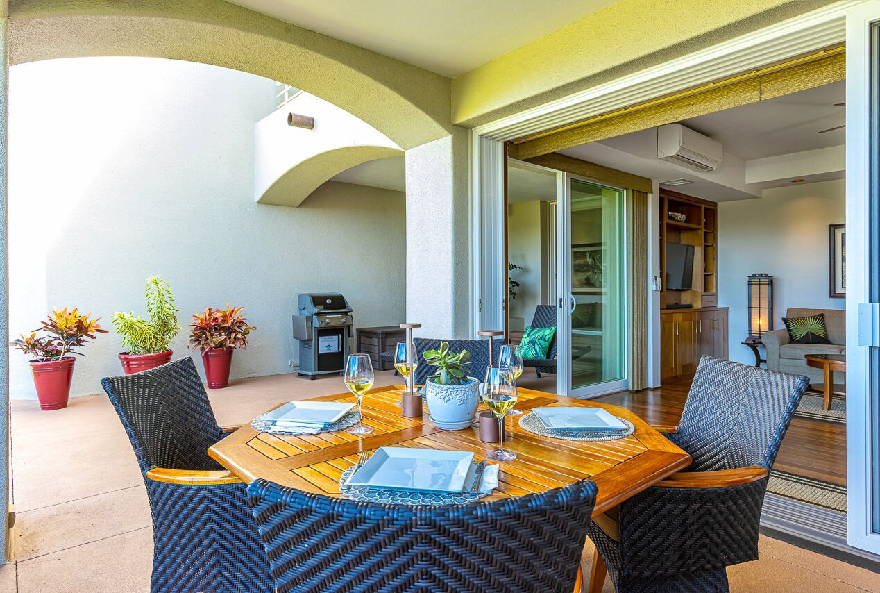 Un coin repas avec une table en bois et des chaises en osier, des plantes en pot et une vue sur le salon.