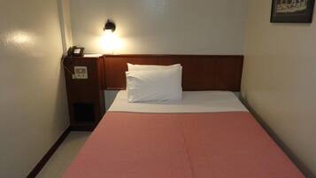 Een eenpersoonsbed met een rode geruite spreidek en een wit kussen in een hotelkamer.