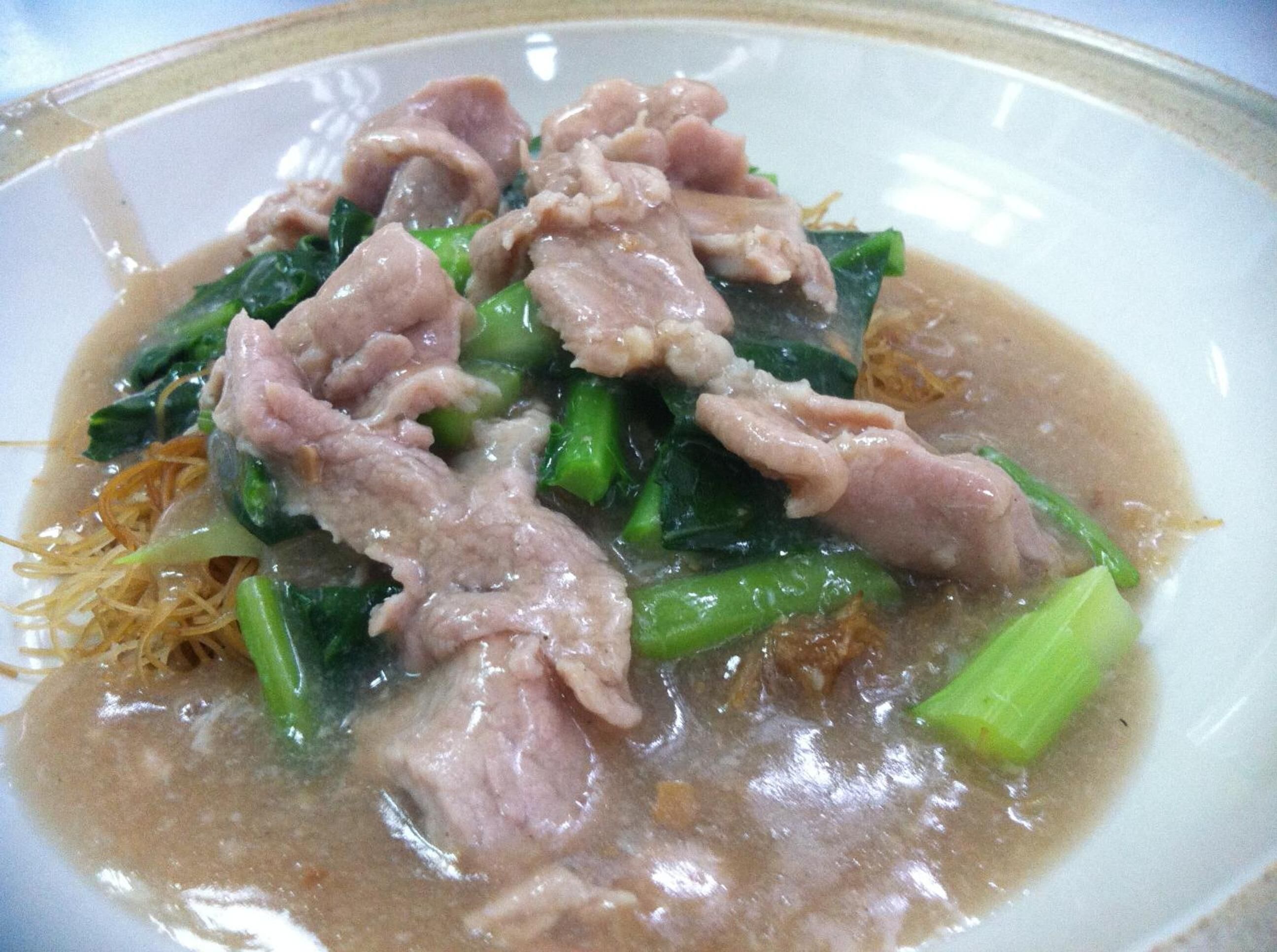 A bowl of soup with meat and greens.