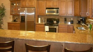 Una cocina con armarios de madera, electrodomésticos de acero inoxidable, encimera de granito y taburetes de bar.