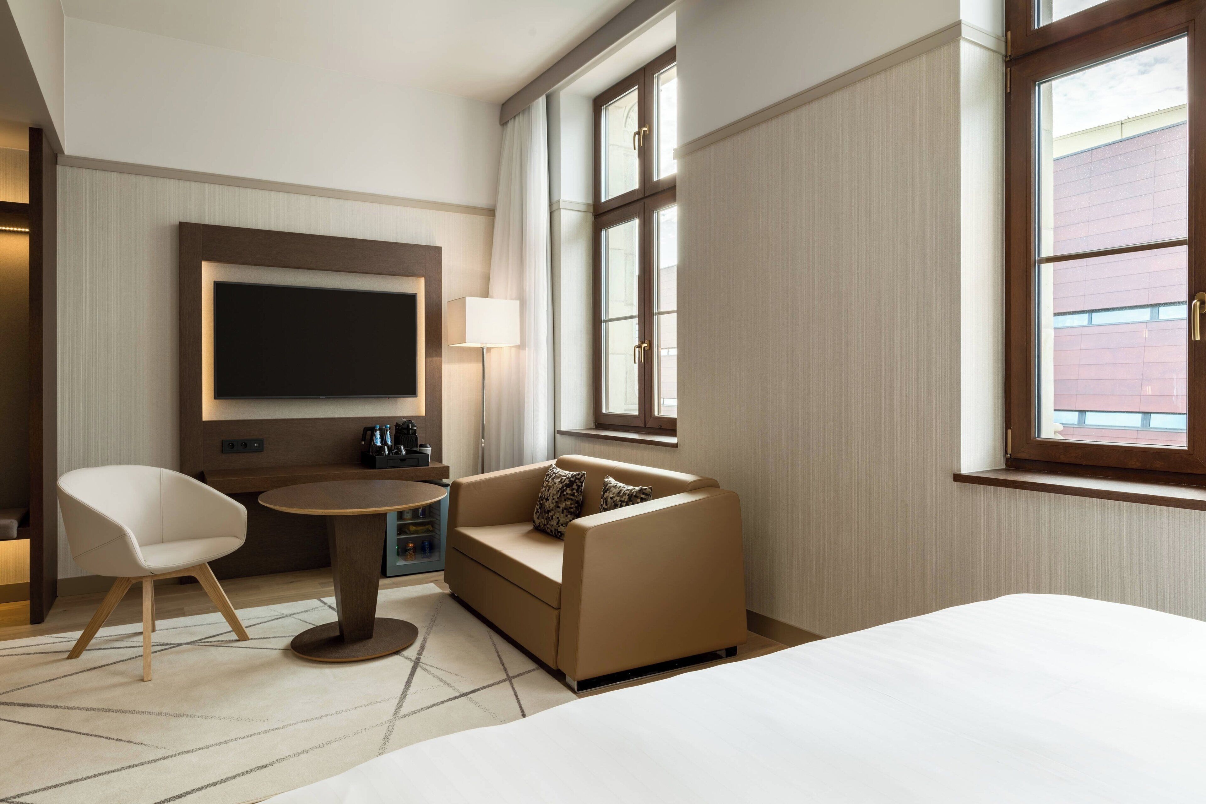 Una habitación de hotel moderna con cama, sofá, televisor, lámpara y ventana con vistas.