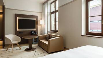 Una habitación de hotel moderna con cama, sofá, televisor, lámpara y ventana con vistas.