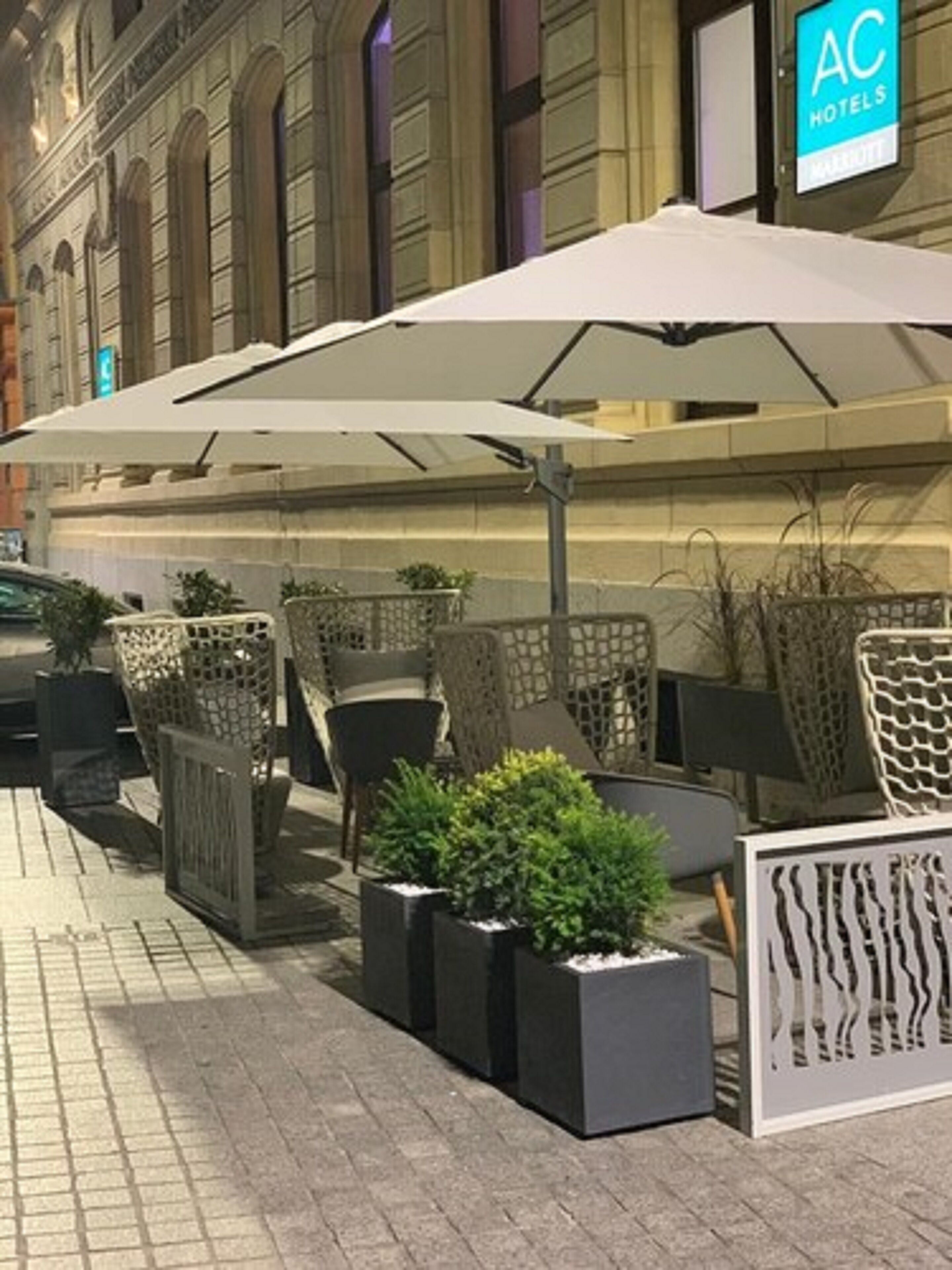 Area esterna con tavoli e ombrelloni, piante in vaso e insegna Marriott AC Hotels.