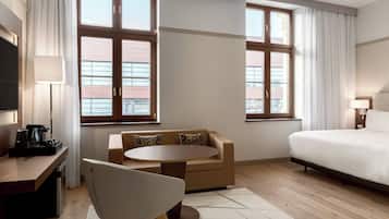 Ein Hotelzimmer mit einem Bett, einem Schlafsofa, einem runden Tisch, einem Schreibtisch mit Lampe und einem Fernseher.