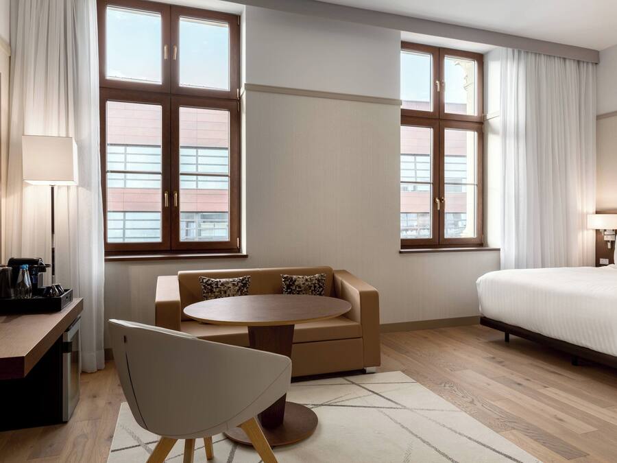 Ein Hotelzimmer mit einem Bett, einem Schlafsofa, einem runden Tisch, einem Schreibtisch mit Lampe und einem Fernseher.