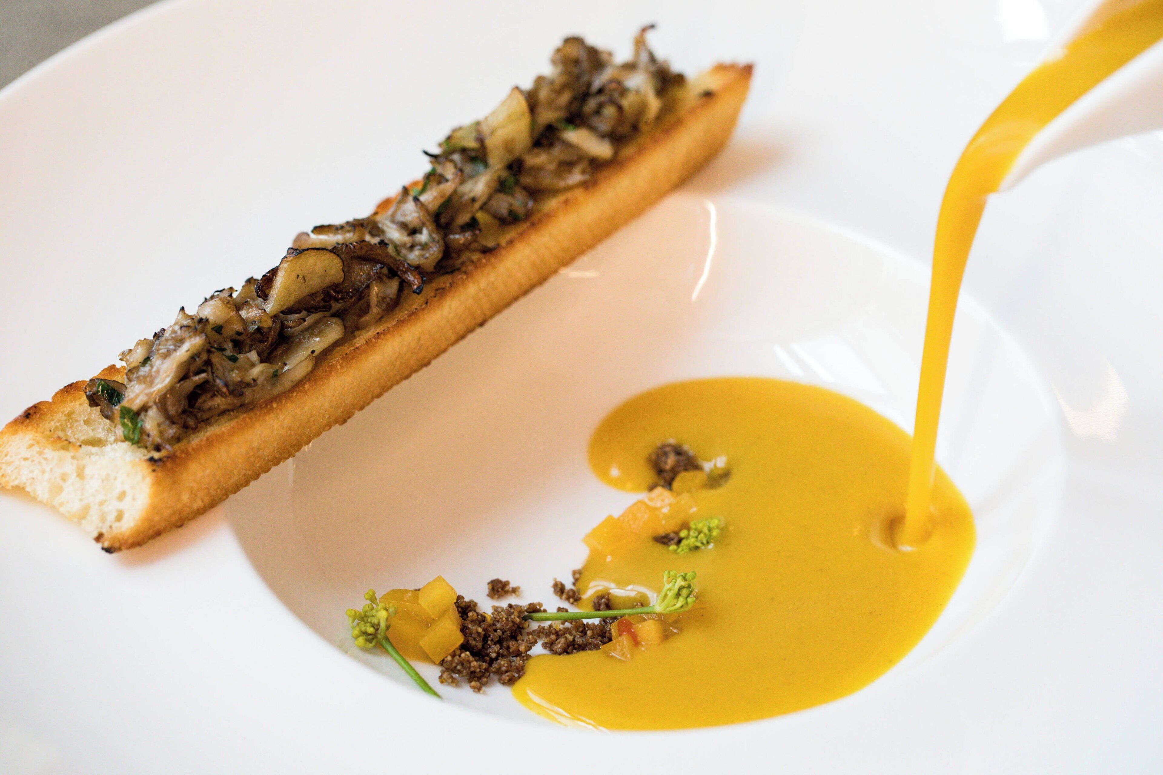 A dish with a bread base topped with mushrooms and a yellow sauce.