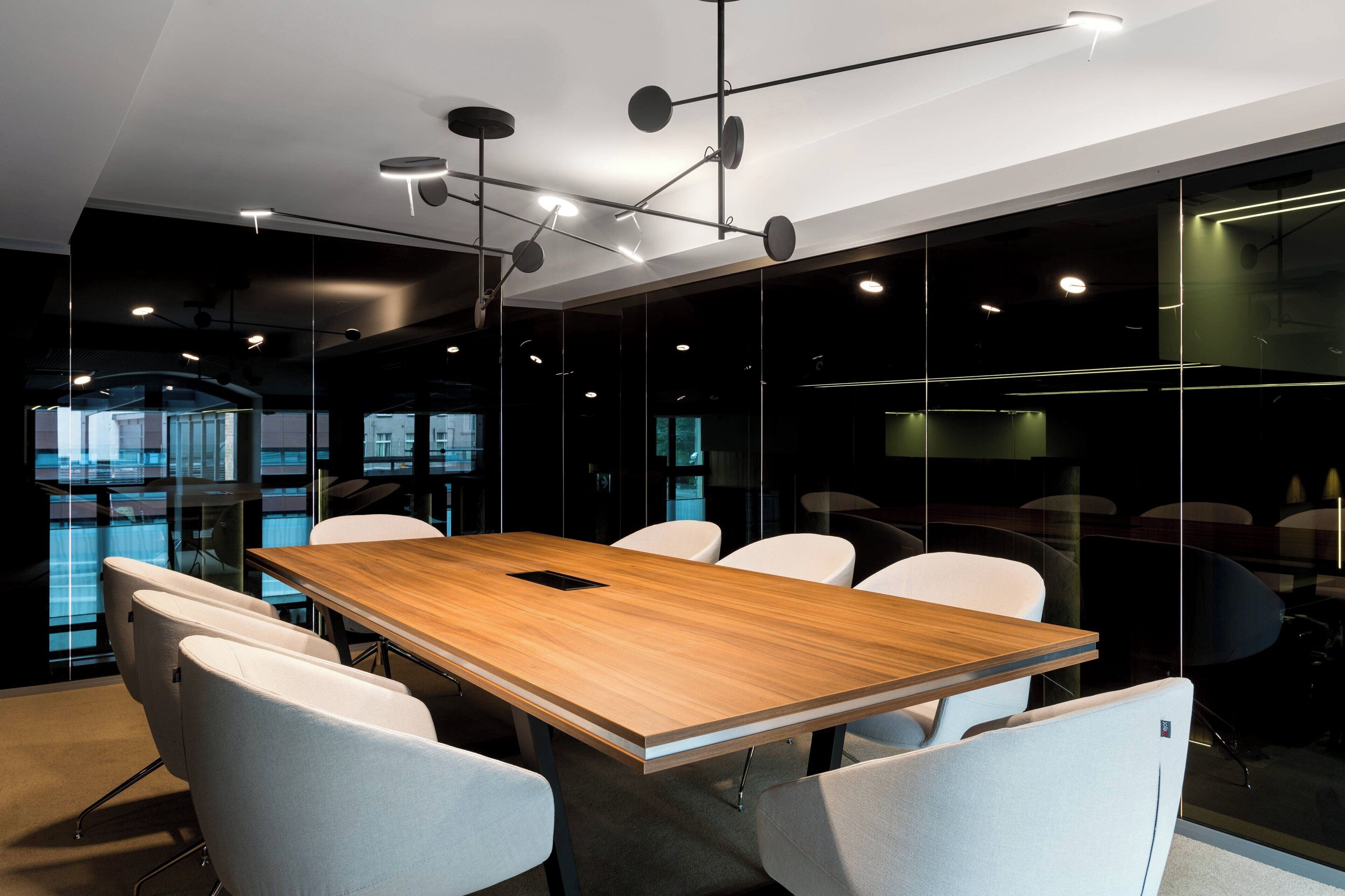A conference room with a wooden table, white chairs, and modern lighting fixtures.