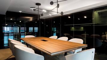 A conference room with a wooden table, white chairs, and modern lighting fixtures.