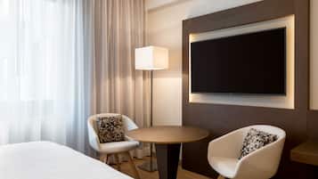 A hotel room with a bed, two chairs, a table, a TV, and a lamp.