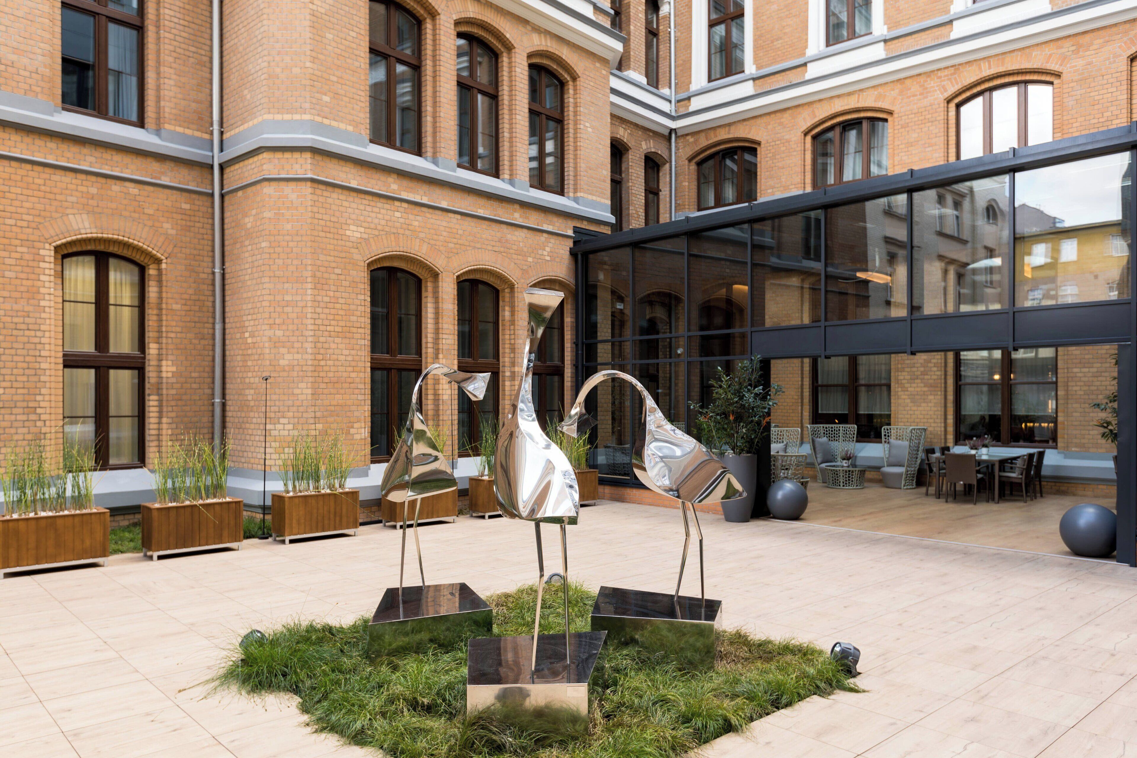 Een binnenplaats met een modern gebouw, terrasmeubels en decoratieve metalen sculpturen.