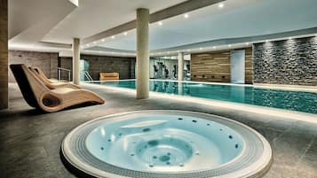 A modern indoor swimming pool area with a hot tub, exercise equipment, and a lounge chair.