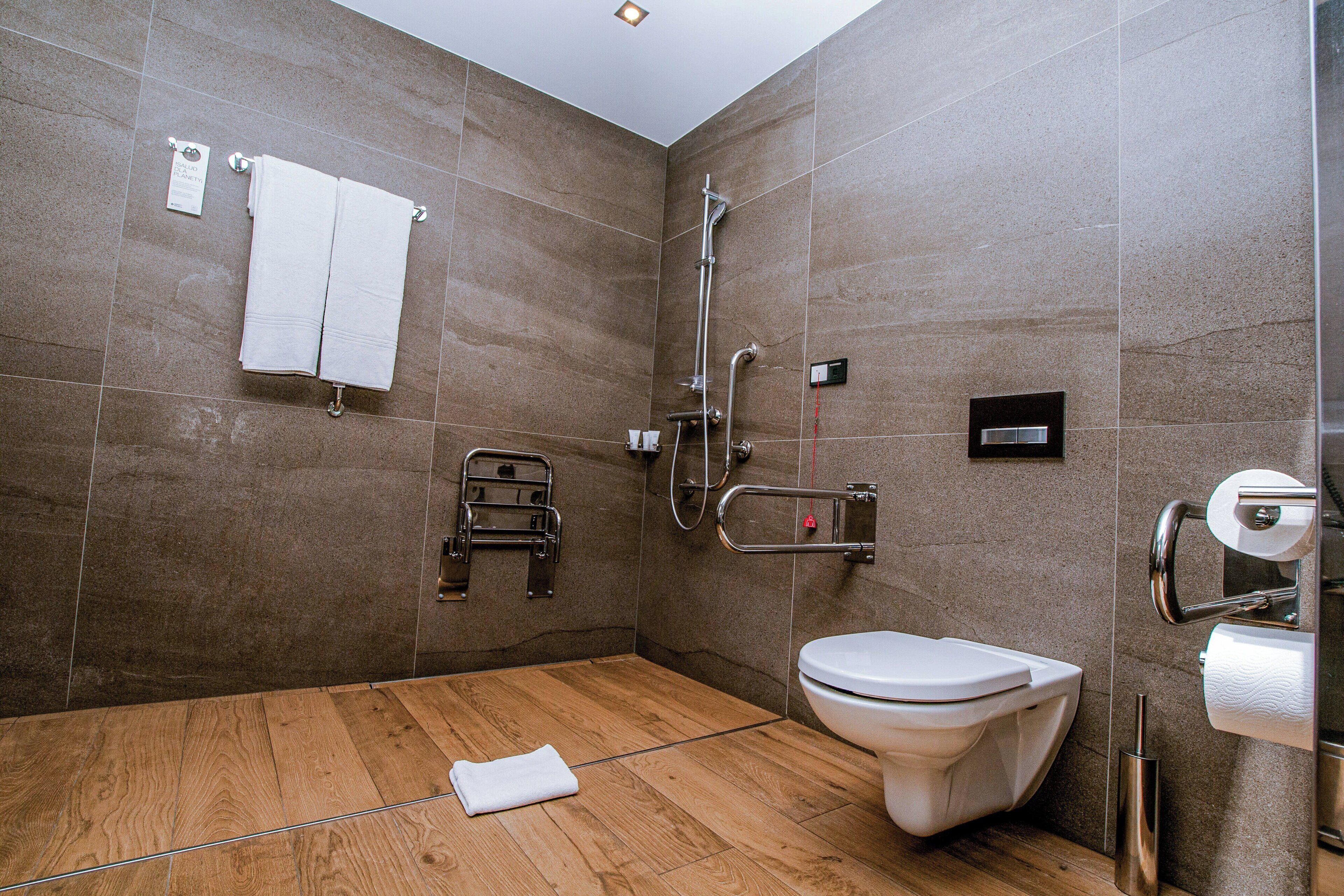 Ein modernes Badezimmer mit Dusche, Toilette und Haltegriffen.