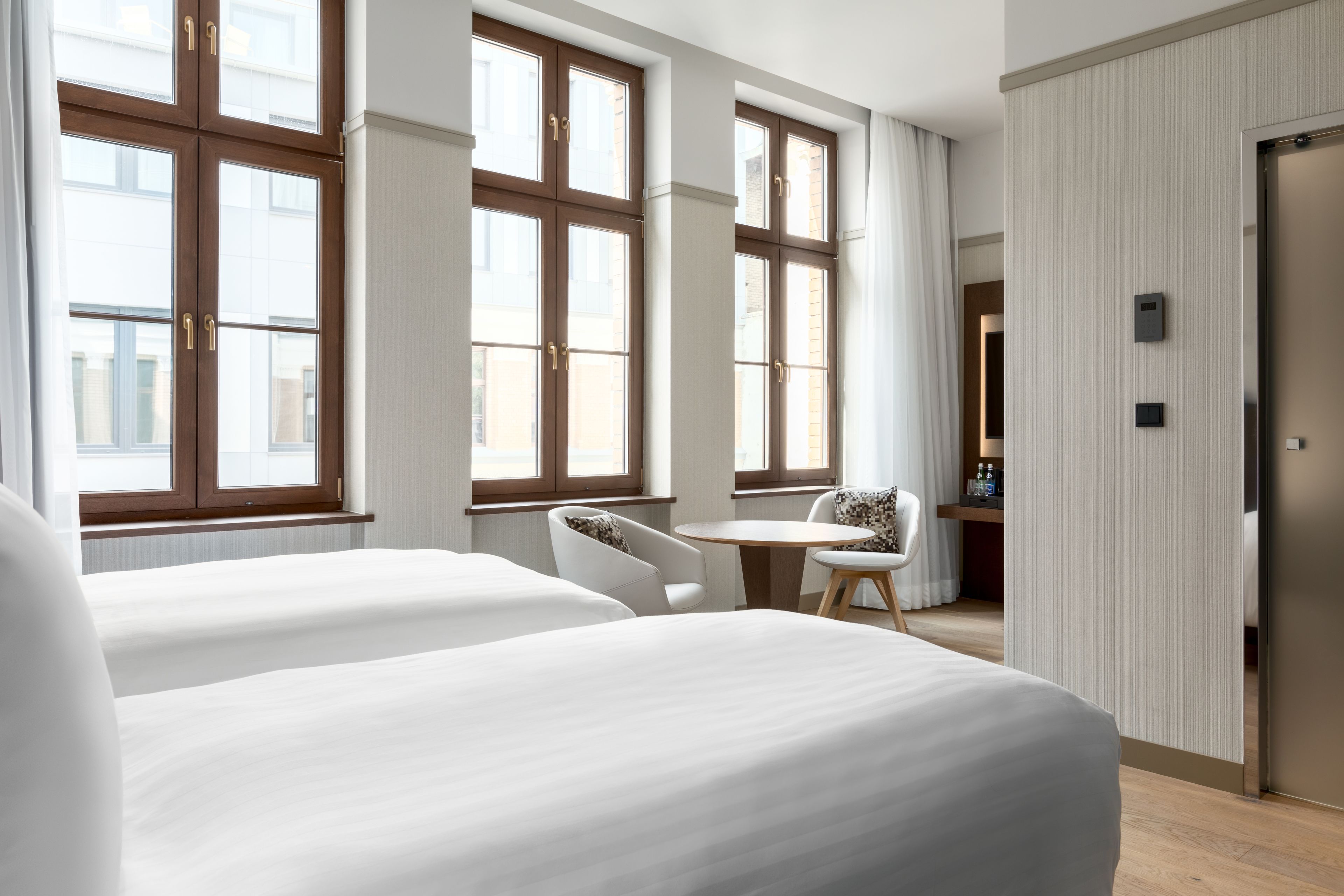 A hotel room with two beds, a small round table, a chair, and a wardrobe.