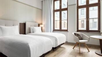 A hotel room with two beds, a chair, a round table, and large windows.