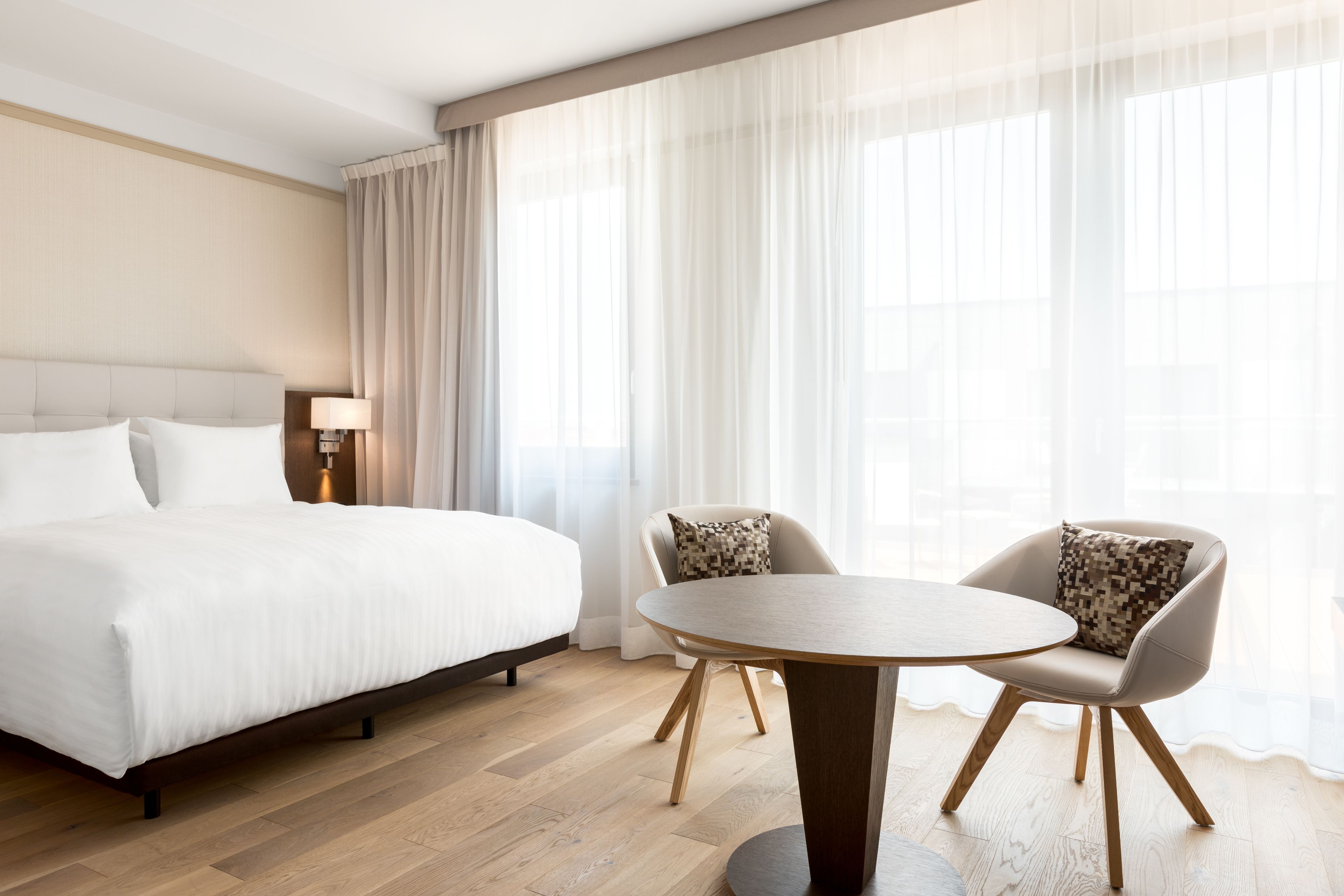 Una habitación de hotel con una cama, una mesa redonda, dos sillas y una mesita de noche con lámpara.