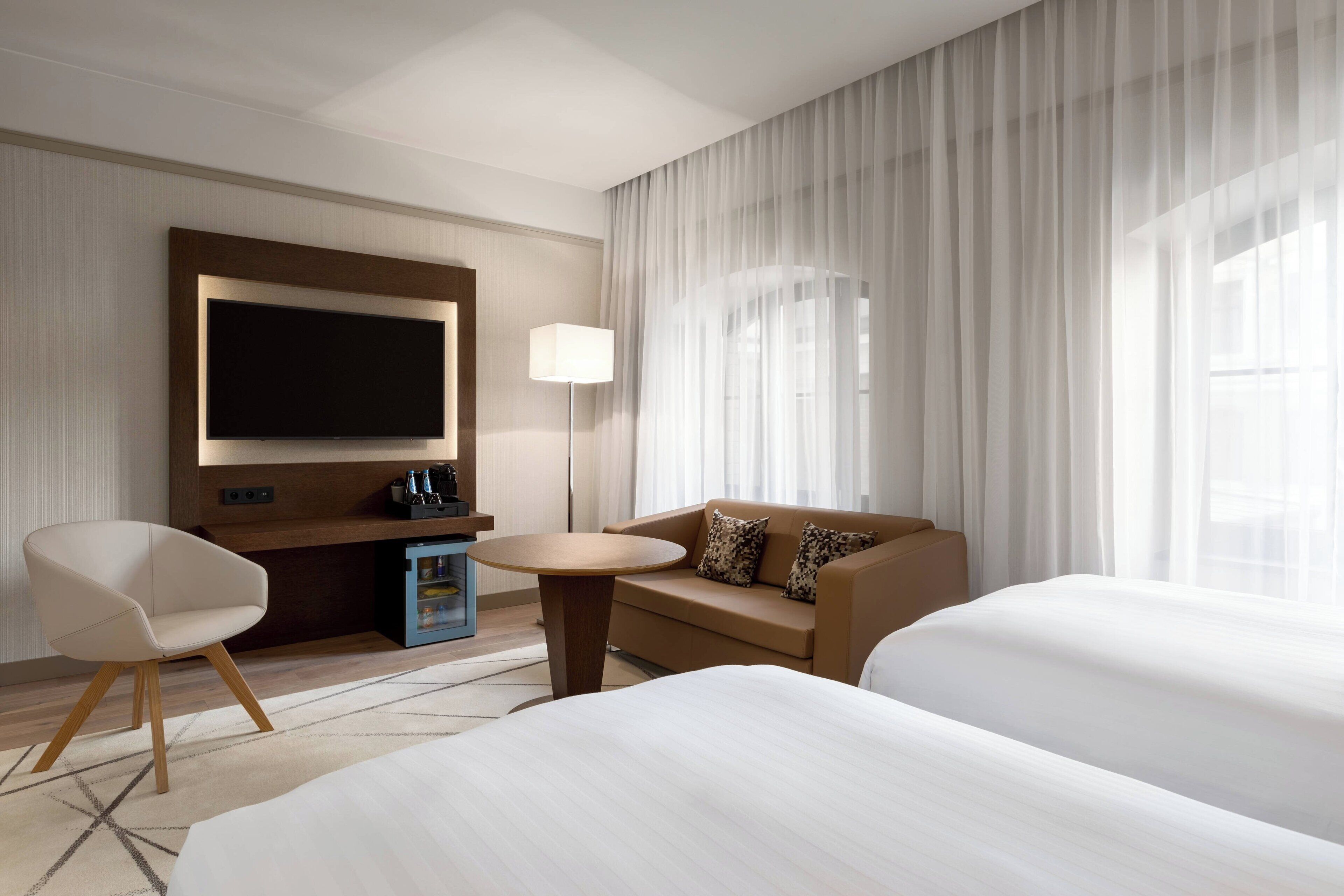 Habitación de hotel con una televisión de pantalla plana grande, un sofá, dos camas, una mesita y una lámpara.