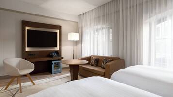 Habitación de hotel con una televisión de pantalla plana grande, un sofá, dos camas, una mesita y una lámpara.
