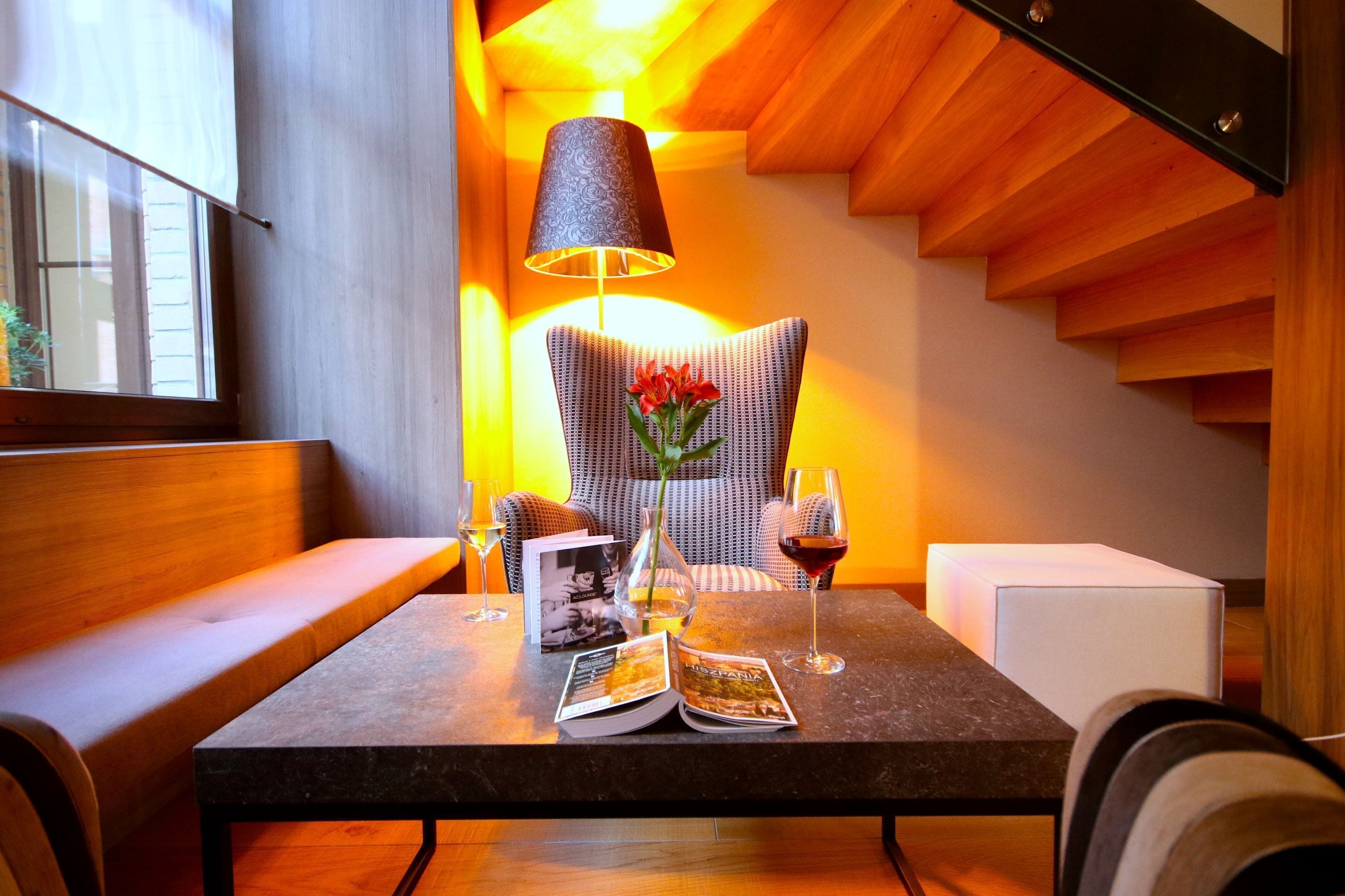 Un coin lecture confortable avec un canapé, une table sur laquelle est posé un magazine, une lampe et deux verres de vin.