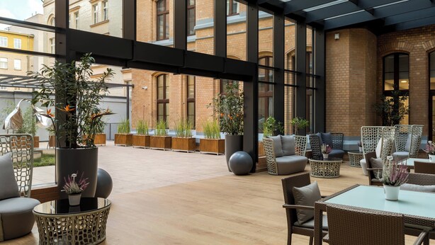 Un área de estar al aire libre con muebles de mimbre, plantas en macetas y una mesa de vidrio.