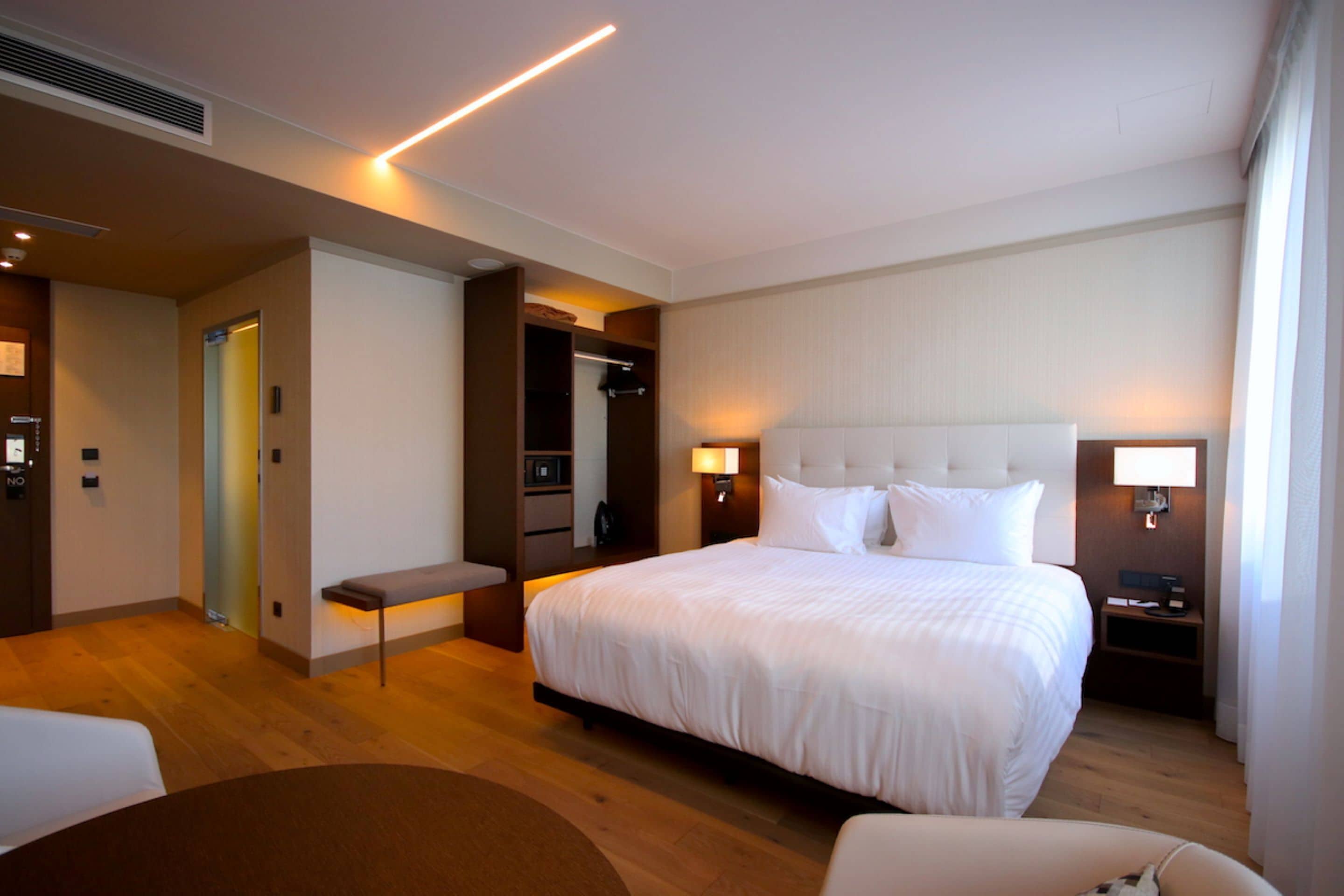 Quarto de hotel com cama grande, mesas de cabeceira, um banco e um closet espaçoso.