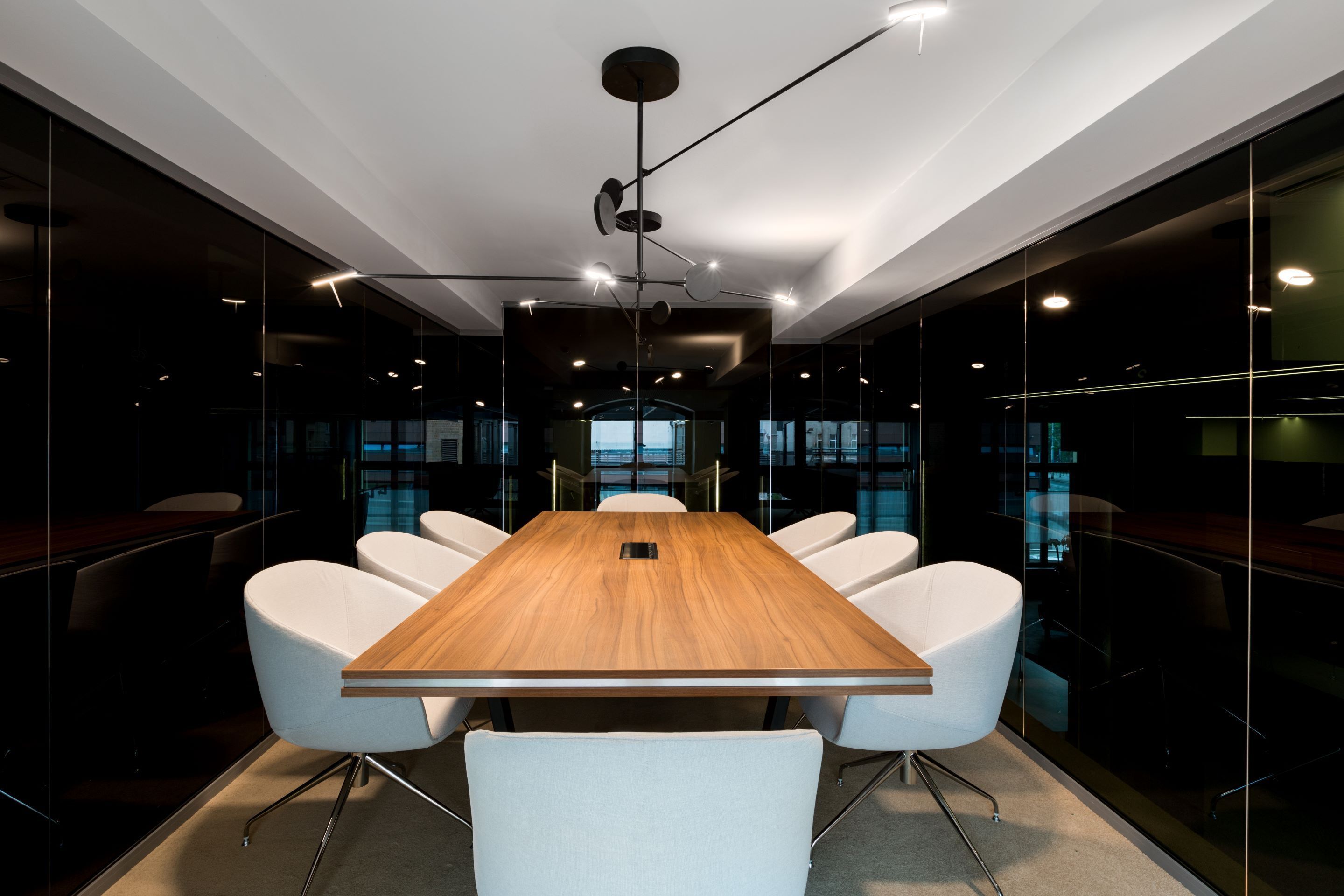 A conference room with a wooden table, white chairs, and modern lighting.