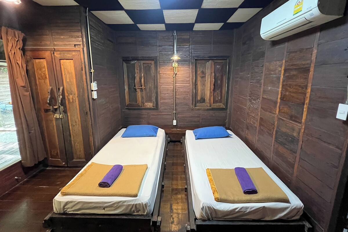 A room with two beds, wooden walls, a checkered ceiling, and an air conditioning unit.