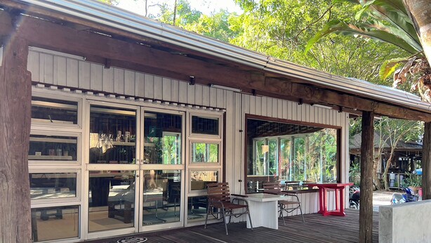 Un espace extérieur abrité, doté d’une terrasse en bois, de grandes fenêtres et d’un coin salon avec des tables et des chaises.