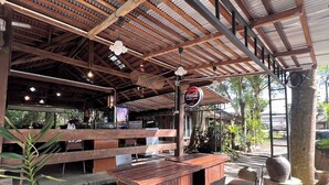 Un restaurant en plein air avec des tables et des chaises en bois, une enseigne Coca-Cola et une enseigne Pepsi.