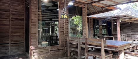 Un edificio de madera rústico con un amplio ventanal y una mesa y banco de madera instalados afuera.